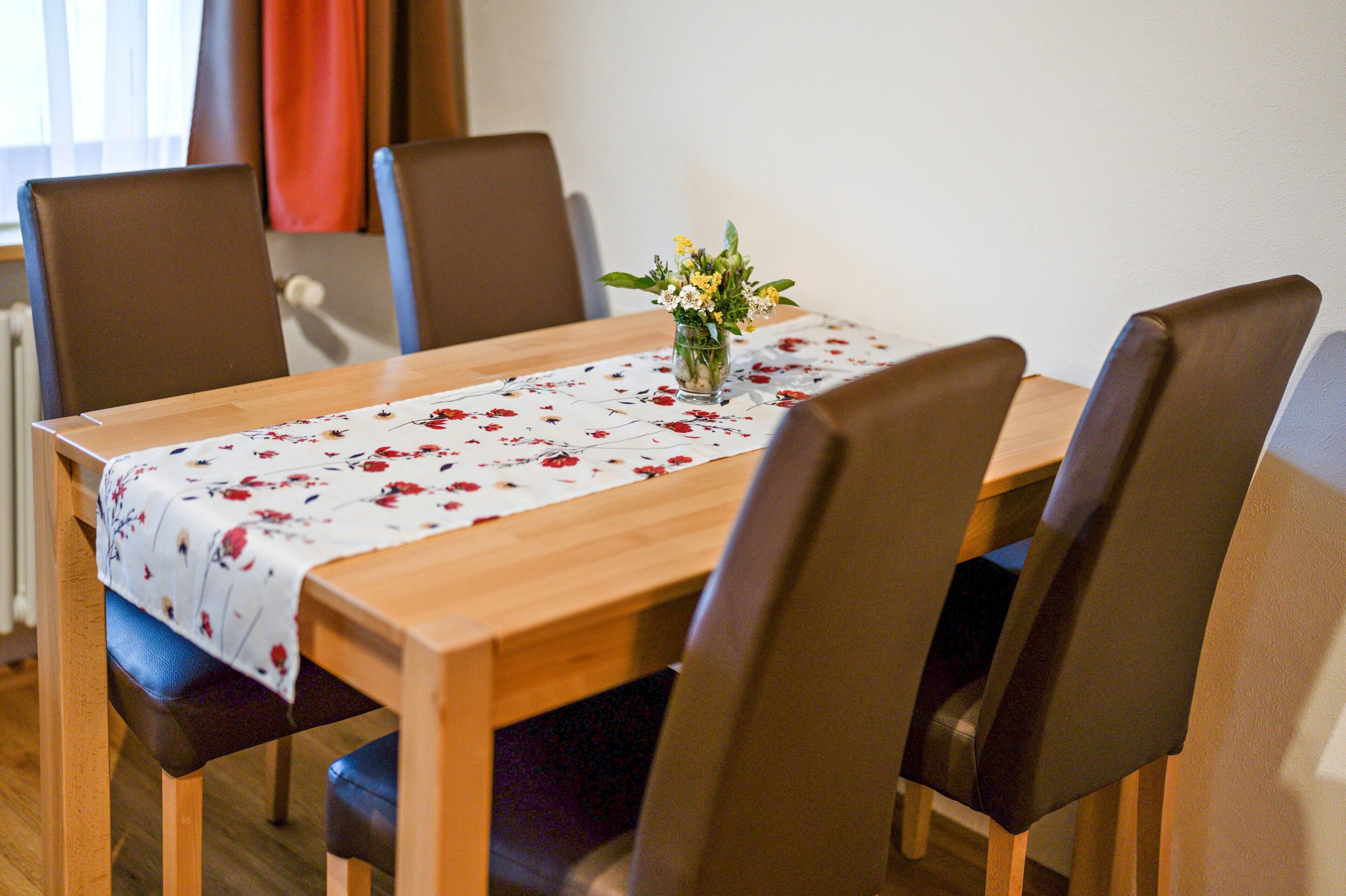 A dining table with a floral tablecloth, surrounded by chairs.