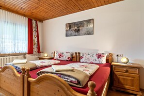 A double bed with floral bedding, a wooden headboard, a nightstand with a lamp, and a painting on the wall.