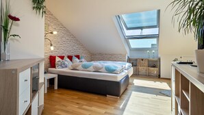 A modern bedroom with a sloped ceiling, a skylight, a bed with patterned bedding, a bedside table, and a wooden dresser.