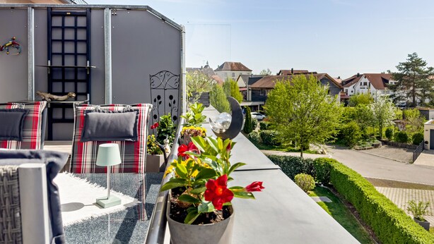 A balcony with outdoor furniture, a potted plant, and a view of a residential street.
