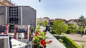 Un balcon aménagé avec du mobilier d’extérieur, un pot de fleurs et une vue sur une rue résidentielle.