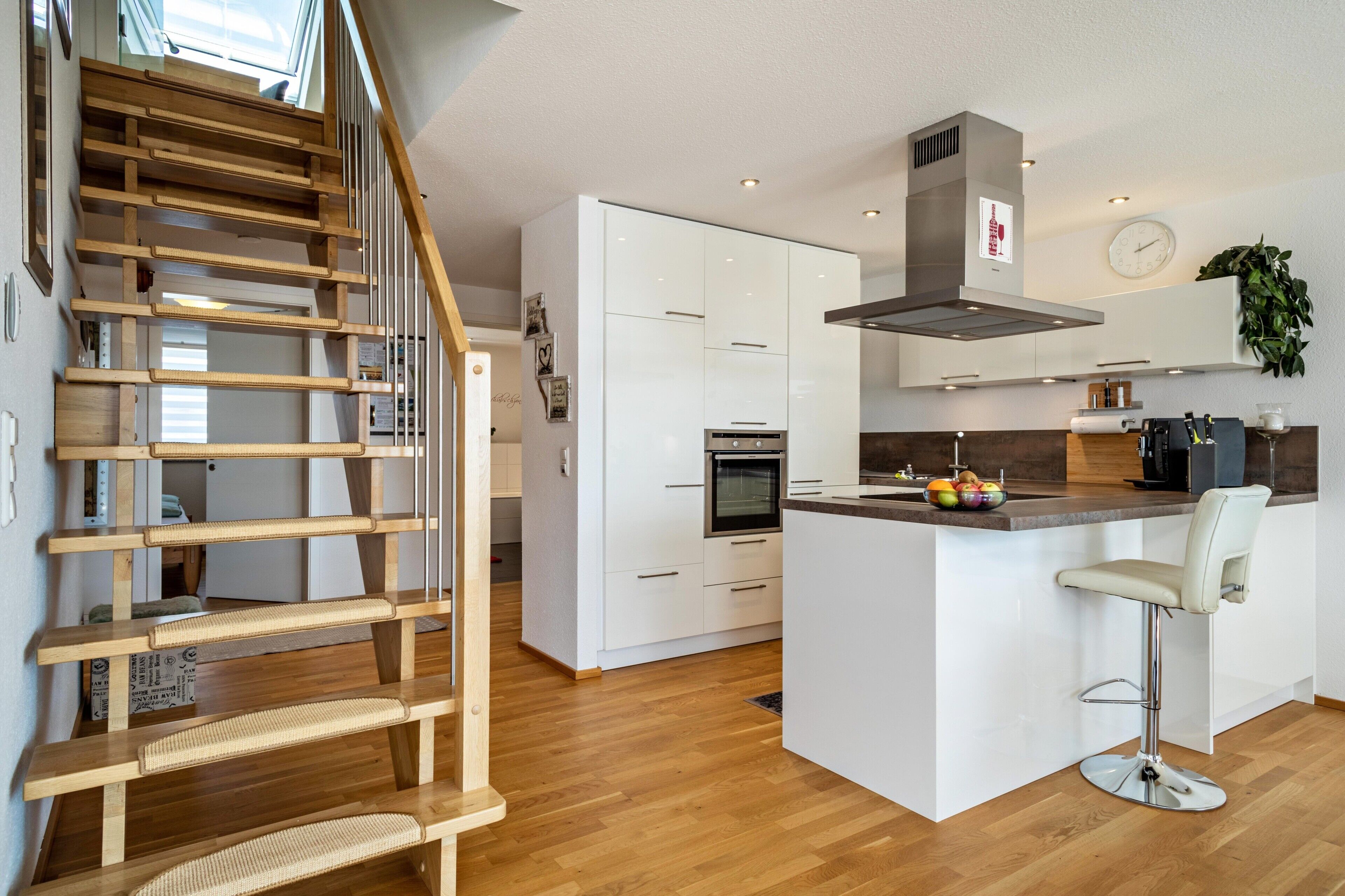 Une cuisine moderne avec des armoires blanches, une hotte de cuisinière en acier inoxydable et un escalier en bois.