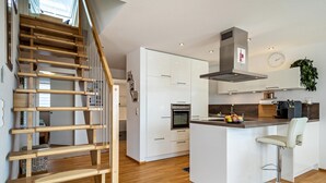 A modern kitchen with white cabinets, a stainless steel range hood, and a wooden staircase.