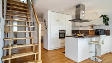 Une cuisine moderne avec des armoires blanches, une hotte de cuisinière en acier inoxydable et un escalier en bois.