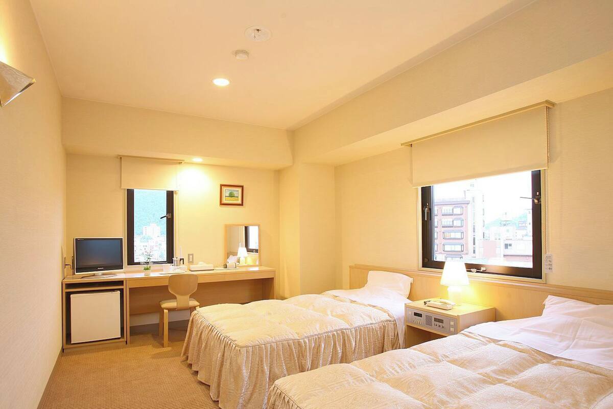 Une chambre d’hôtel avec deux lits, un bureau avec un ordinateur, une chaise et un petit réfrigérateur.