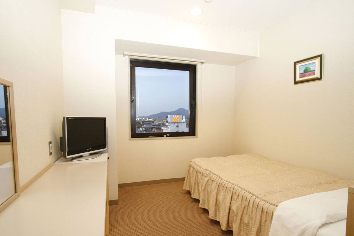 Une chambre d’hôtel avec un lit, un bureau avec une télévision, une fenêtre donnant sur la ville et un tableau encadré au mur.