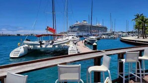 Un puerto deportivo con barcos amarrados, un crucero y una terraza de madera con sillas blancas.