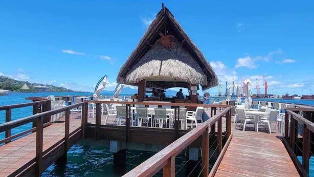Estructura con techo de paja y asientos al aire libre sobre un muelle.