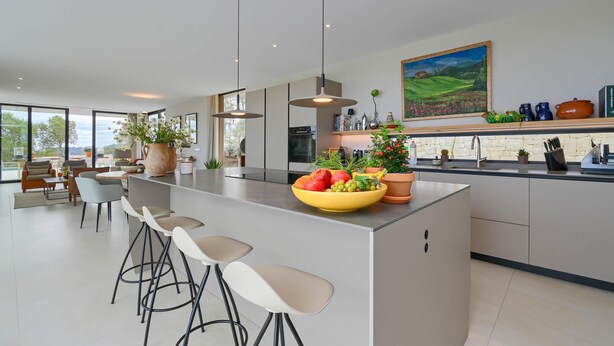 Une cuisine moderne dotée d’un grand îlot central, de tabourets de bar et d’un panier à fruits.