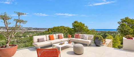 An outdoor seating area with a sofa, chairs, and a coffee table, overlooking a scenic landscape.