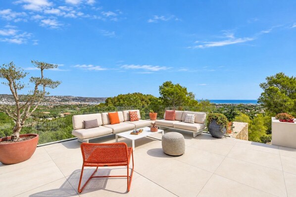 An outdoor seating area with a sofa, chairs, and a coffee table, overlooking a scenic landscape.
