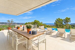 A terrace with a wooden table, white chairs, and a view of the sea.