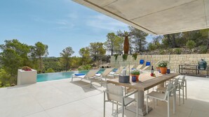 Une terrasse extérieure avec une piscine, des chaises longues, une table à manger et un mur en pierre en arrière-plan.
