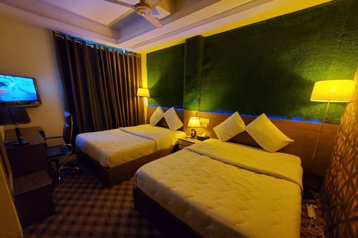 A hotel room with two beds, a desk, a chair, a television, and a wall-mounted lamp.