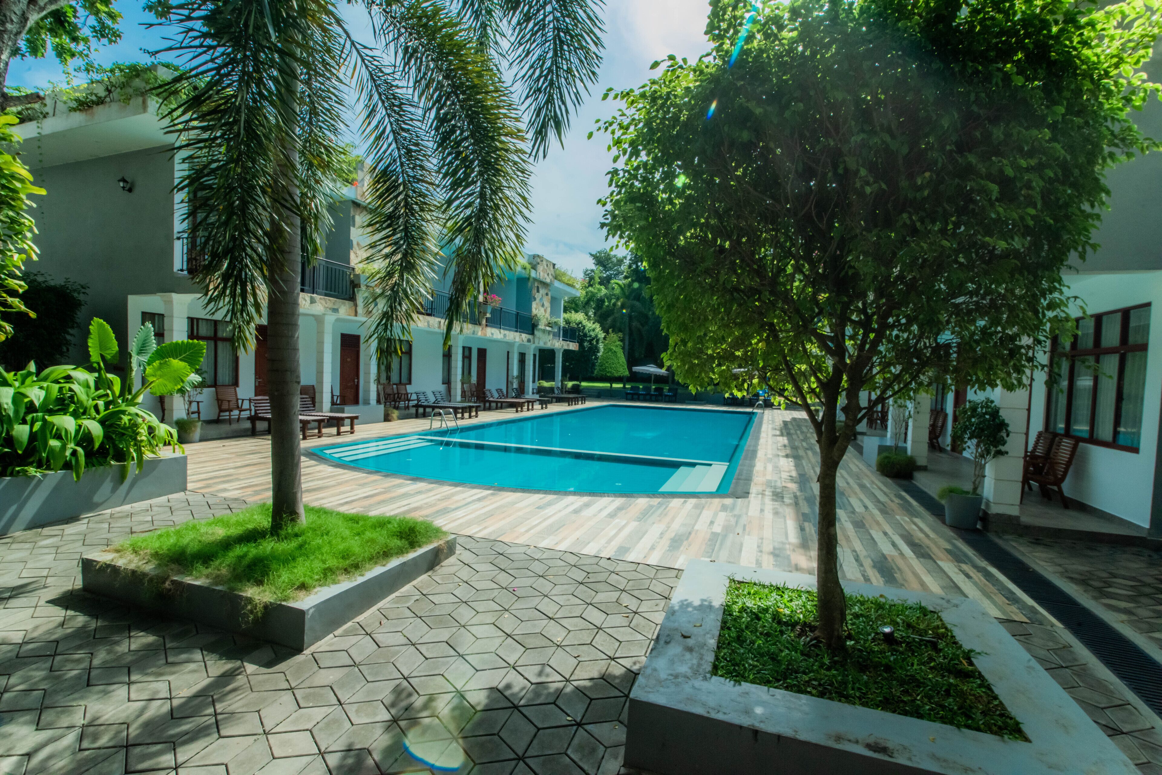 A swimming pool surrounded by a tiled patio with planters and trees.