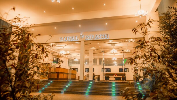 The entrance to a hotel named "ROYAL & REACH" with a reception desk, a staircase, and decorative lighting. - Royal Reach Udawalawe (Udawalawa)