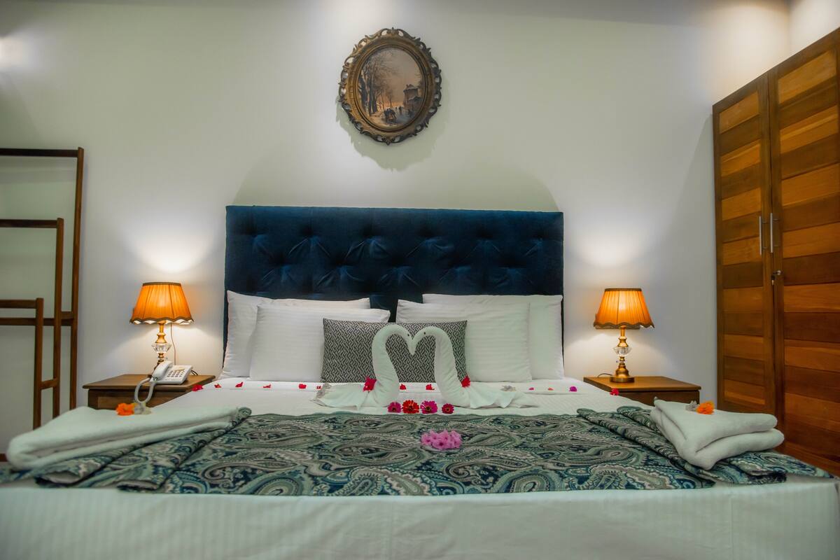 Una cama bien hecha con un cabecero azul, dos lámparas de noche y un cuadro en la pared.