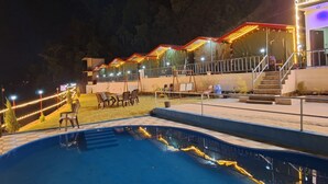 A swimming pool with lounge chairs and a covered seating area with lights.