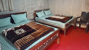 A room with two beds, each with patterned bedding and a wooden headboard. There is a red carpet on the floor and a chair in the corner.