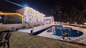 A hotel with a swimming pool, outdoor seating, and a well-lit building facade.