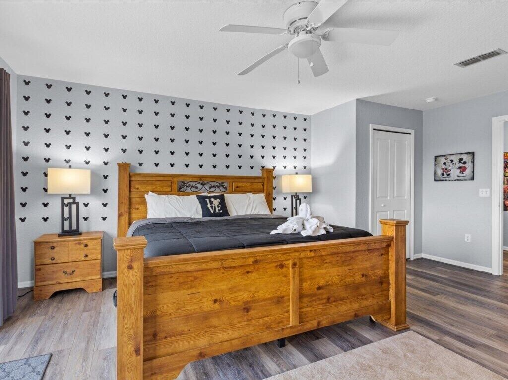 A bedroom with a wooden bed, two bedside tables, a ceiling fan, and a wall with heart-patterned wallpaper.