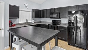 Eine moderne Küche mit dunklen Schränken, einem Edelstahlkühlschrank, einer Mikrowelle und einer Arbeitsplatte aus Granit.