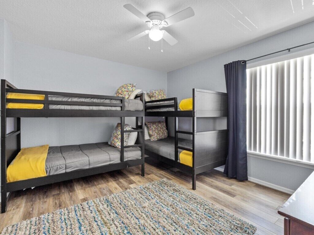 A bunk bed room with a ceiling fan, a window with curtains, and a patterned rug.
