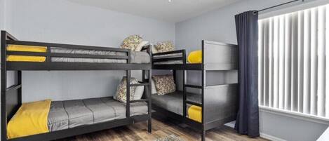 A bunk bed room with a ceiling fan, a window with curtains, and a patterned rug.