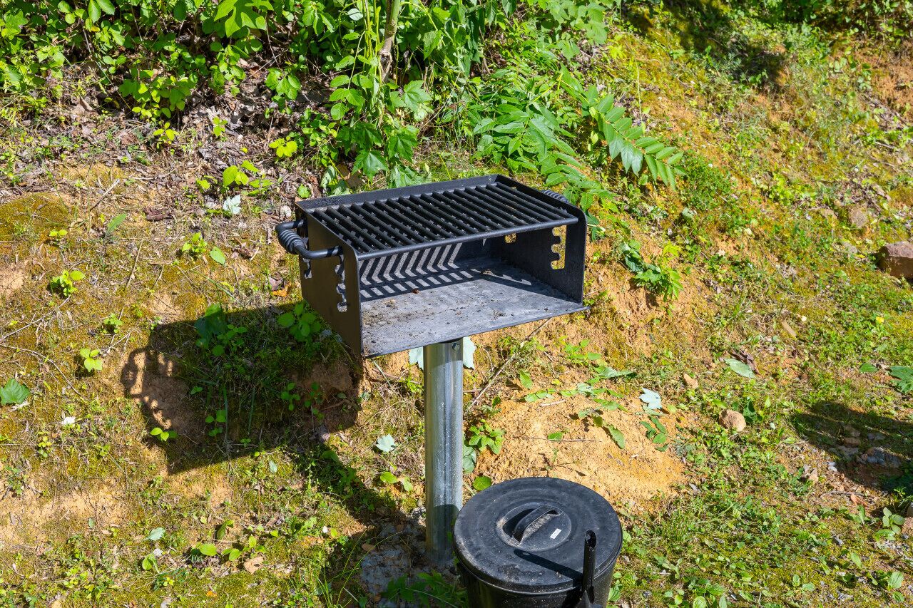 A metal structure with a grill and a black container, possibly for food storage, in a natural outdoor setting.