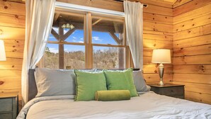 Une chambre à coucher dans une cabane en bois, avec un lit, des oreillers, une table de chevet avec une lampe et une fenêtre avec des rideaux.