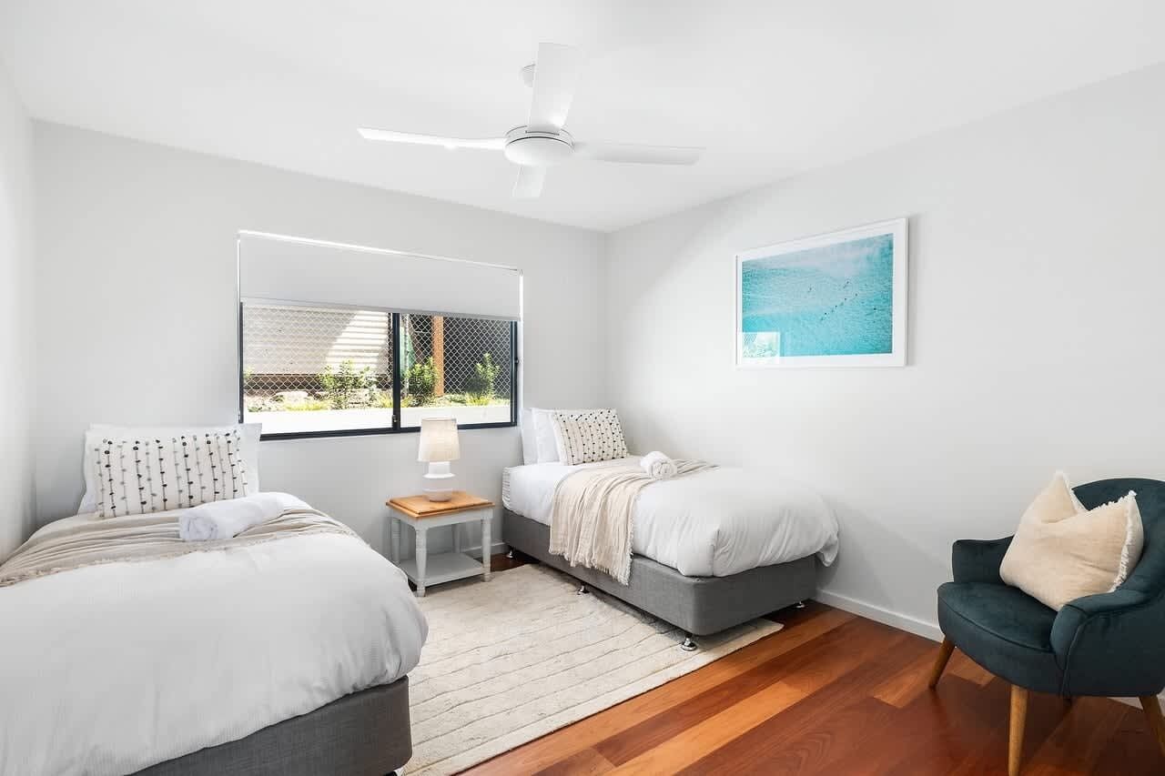 A bedroom with two beds, a ceiling fan, a window with a view, and a chair.