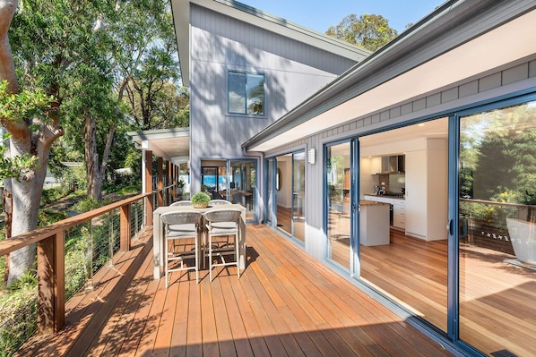 A modern house with a deck, large windows, and a kitchen visible through the glass.
