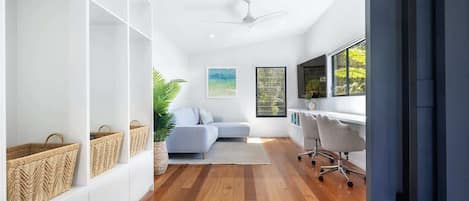 A modern living room with a sofa, a desk, and a chair. There are baskets on shelves and a plant.