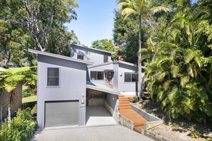 Ein modernes, zweistöckiges Haus mit Garage, umgeben von üppigem Grün und Bäumen.