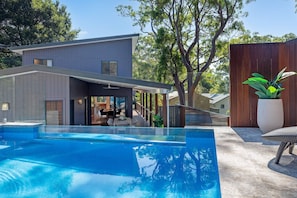 A modern house with a swimming pool, a covered outdoor area, and a wooden fence.