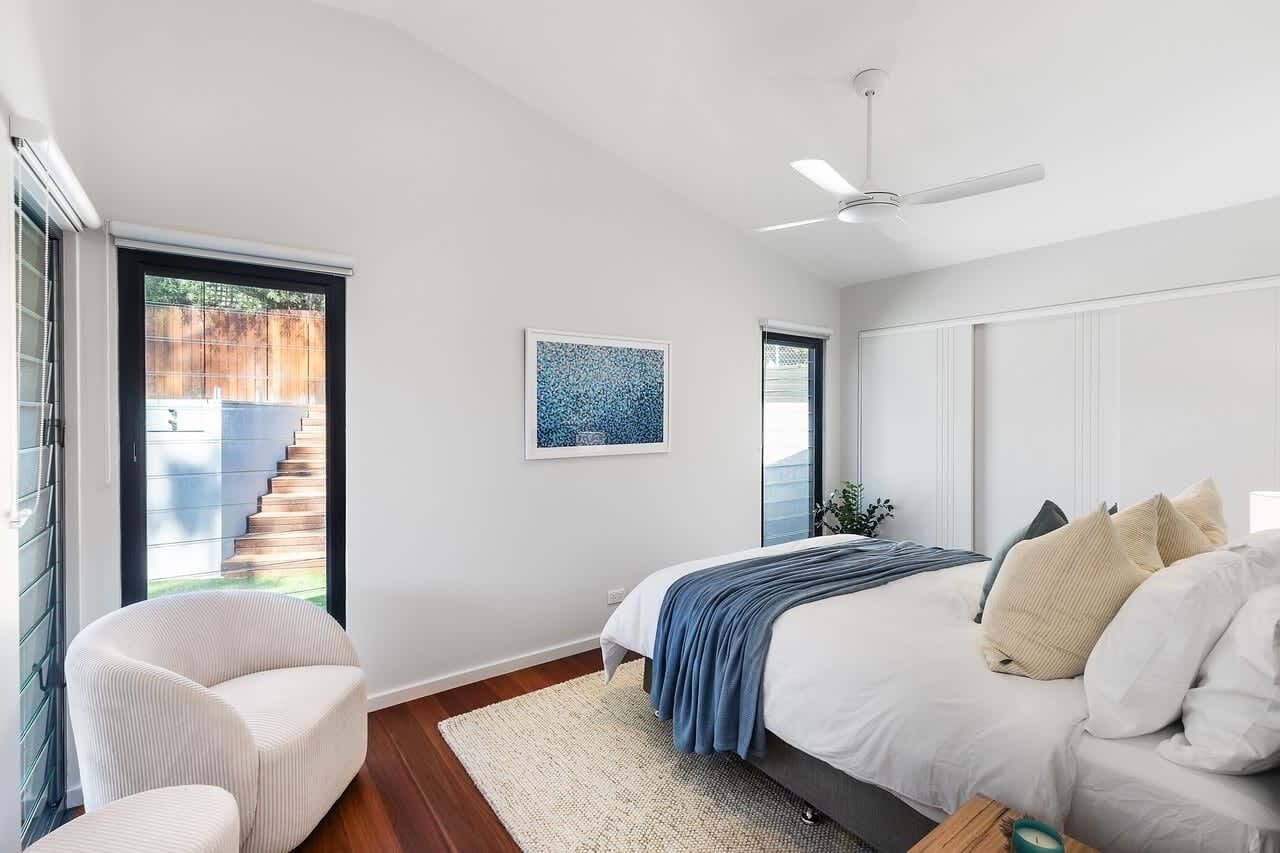 Ein Schlafzimmer mit einem Bett, einem Sessel, einem Deckenventilator und einem Fenster mit Blick auf eine Treppe.