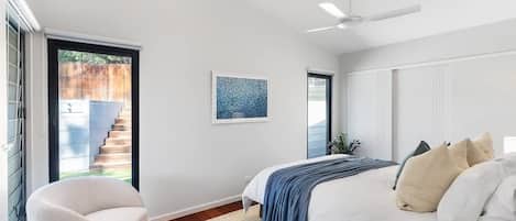 Ein Schlafzimmer mit einem Bett, einem Sessel, einem Deckenventilator und einem Fenster mit Blick auf eine Treppe.