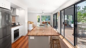 Une cuisine moderne dotée d’un îlot central, d’appareils électroménagers en acier inoxydable et d’une porte-fenêtre coulissante donnant sur une terrasse extérieure.