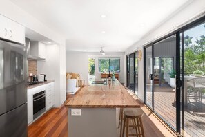 Eine moderne Küche mit Kochinsel, Edelstahlgeräten und einer Glastür, die auf eine Terrasse im Freien führt.