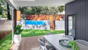 Une terrasse extérieure moderne, dotée d’une plateforme en bois, d’une piscine et d’un espace repas avec des chaises et une table.
