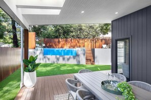 Eine moderne Terrasse im Freien mit Holzdeck, Pool und Essbereich mit Stühlen und Tisch.