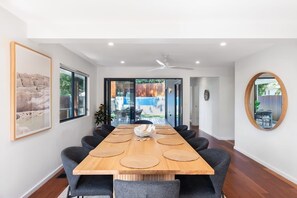 Een moderne eethoek met een lange tafel, stoelen en een plafondventilator.