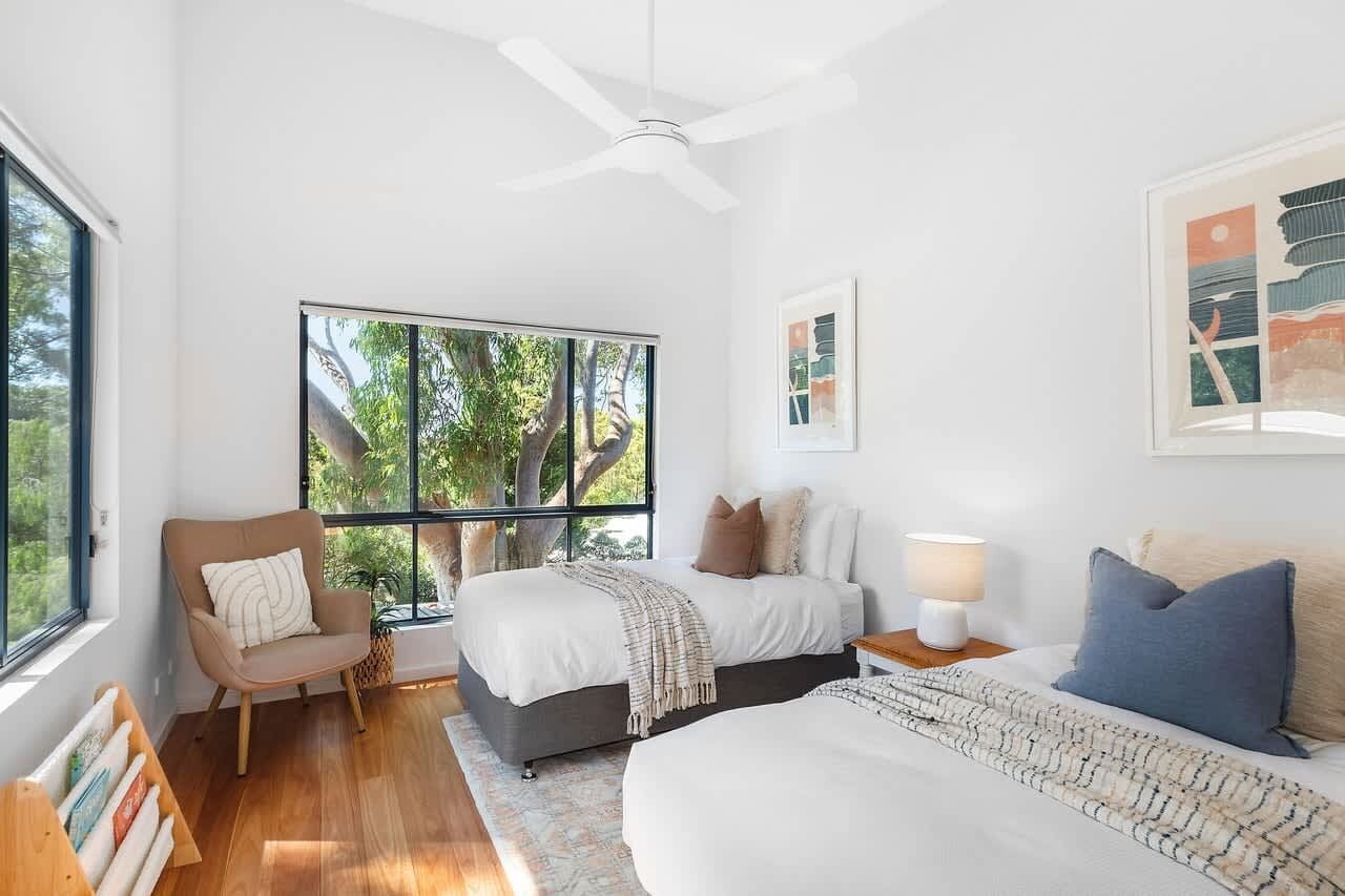A bedroom with a bed, a chair, a nightstand, a ceiling fan, and a window with a view of trees.