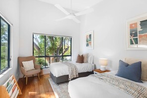 A bedroom with a bed, a chair, a nightstand, a ceiling fan, and a window with a view of trees.