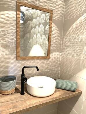 A bathroom with a sink, mirror, and woven basket, set against a brick-patterned wall.