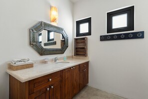 A bathroom with a wooden vanity, a large decorative mirror, a wall-mounted light, and a window with a black frame.