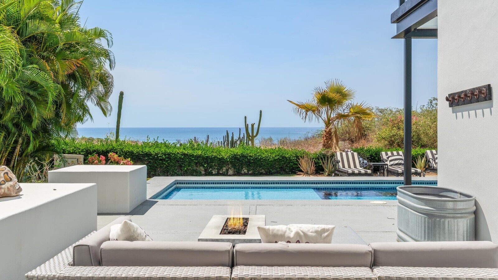 A pool area with a view of the ocean, outdoor seating, and a cactus plant.
