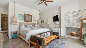 Een slaapkamer met een bed, een bank, een open haard, een televisie en een plafondventilator.