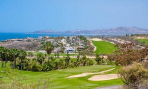 A golf course with a view of the ocean and a residential area in the background.