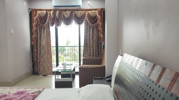 A hotel room with a bed, a chair, a small table with a remote control, and a balcony with curtains. - Hotel Sea Sand (Kanthi)